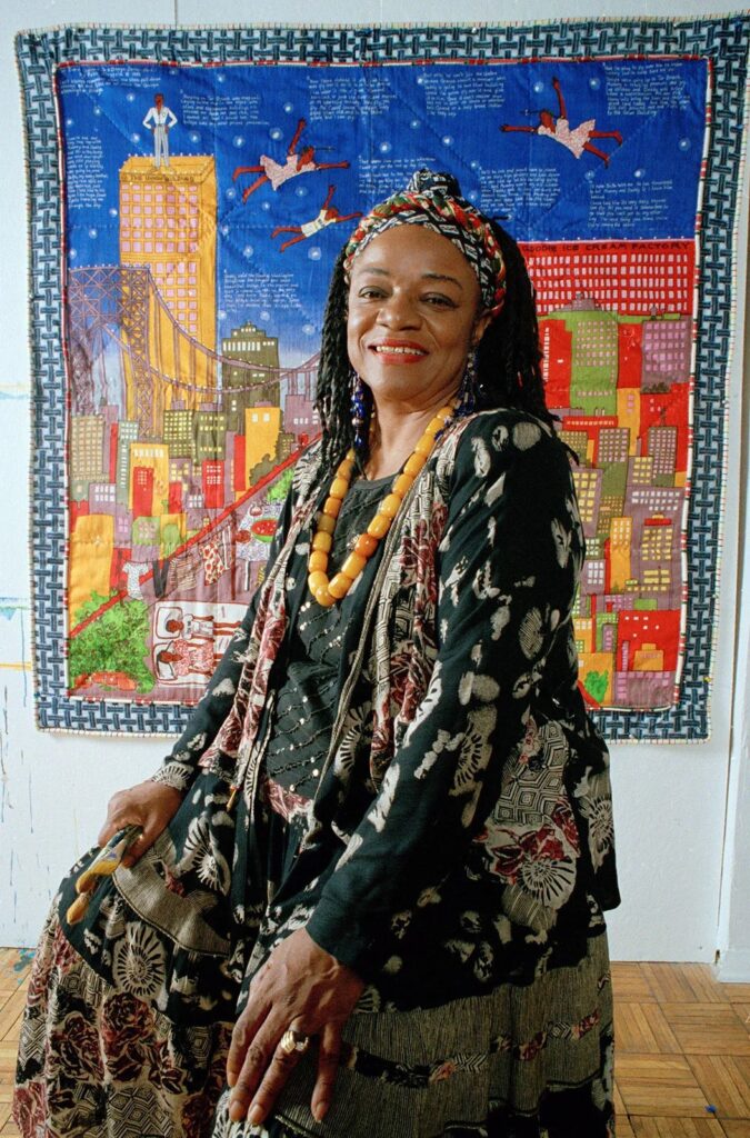 Faith Ringgold Quilt: Faith Ringgold in front of her quilt Tar Beach #2 (1990), 1993. Brittanica.
