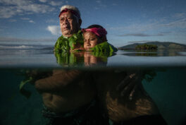 Photo showing an older man with a young boy standing in the water.